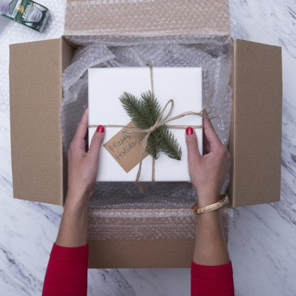 A wrapped gift being placed in a shipping box.