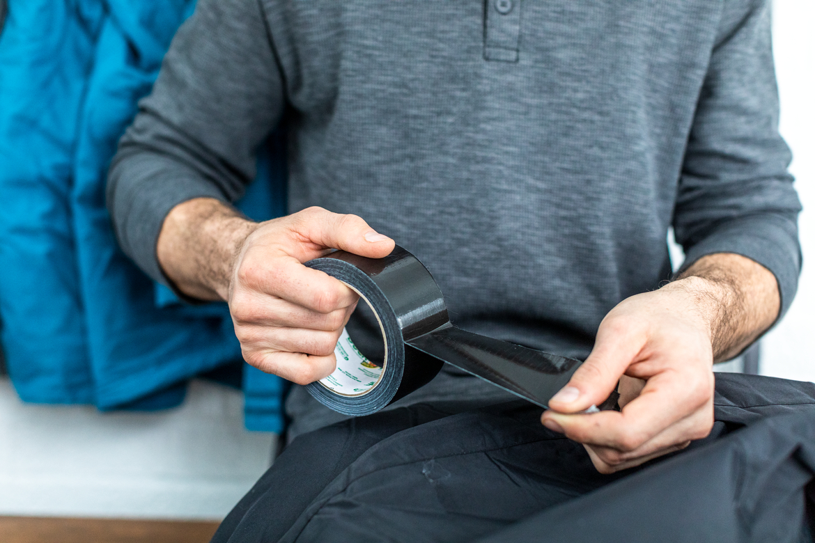 Man repairing black ski paints with black duct tape