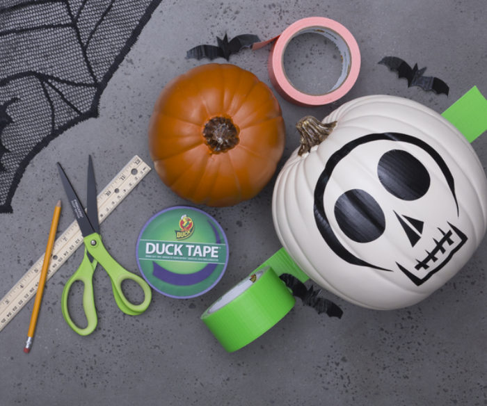 A orange and white pumpkin surrounded by scissors and rolls of Duck Tape.