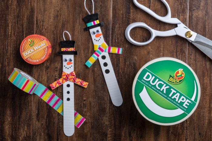 Popsicle stick snowman next to rolls of Duck Tape and scissors