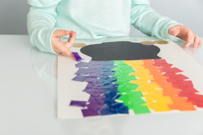 A child creating a picture with a  pot of gold with a colored duck tape rainbow on it.