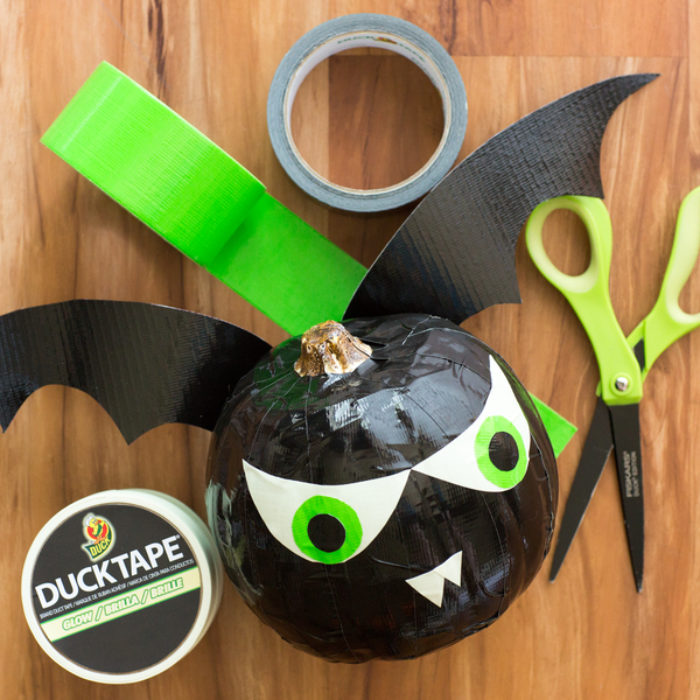 A small black pumpkin decorated as a bat with black and green Duck Tape.