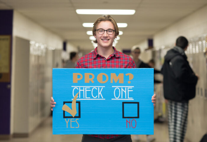 Male student holding a promposal poster made out off duct tape that allows his date to check yes or no.
