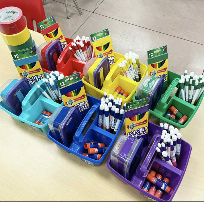 Bins on a table that are red, yellow, green, light blue, dark blue and purple filled with coloring supplies