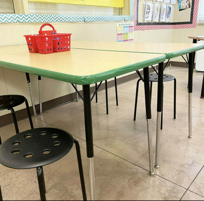 A classroom desk with black chairs and green duck tape around the table edges