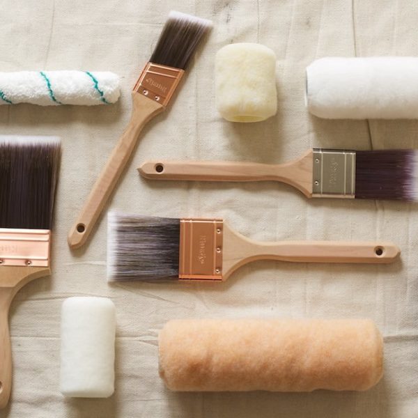 An assortment of paint brushes and rollers on a drop cloth.