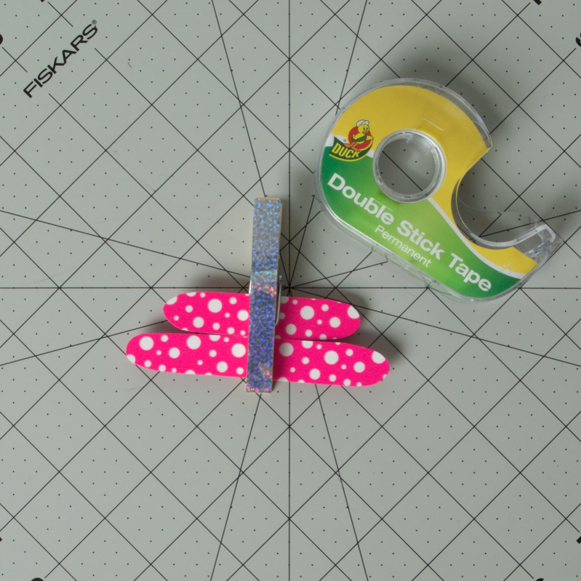 double stick tape applied to the center of each wing from the previous step. Wings are then placed into the clothes pin