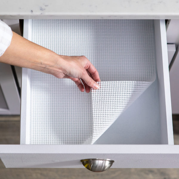 Hand lifting corner of white shelf liner in drawer