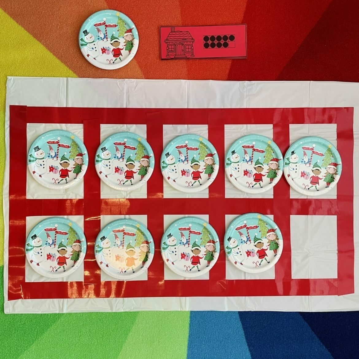 Rectangular white tablecloth with red duct tape and holiday paper plates on a rainbow background for 10 frame