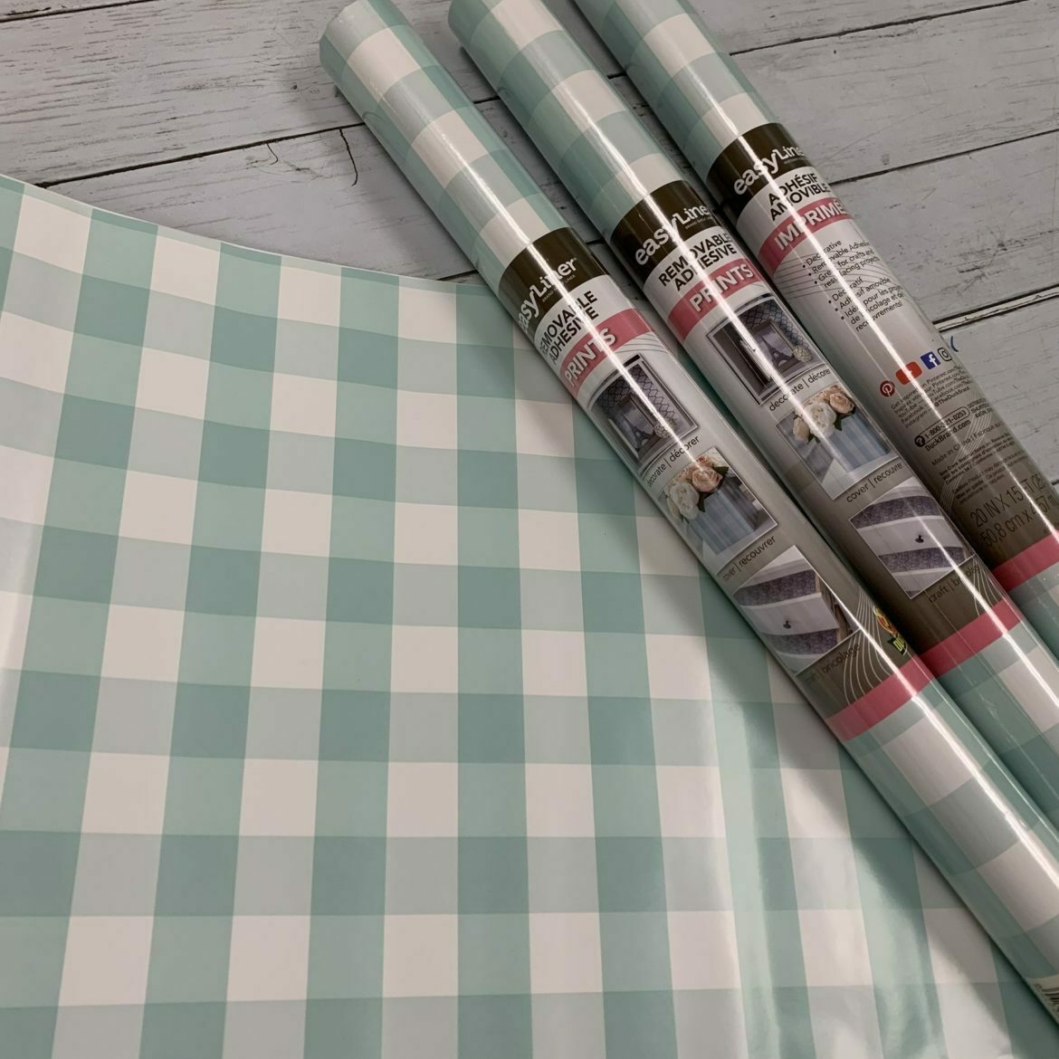 Three rolls of blue checkered shelf liner on top of a sheet of blue checkered shelf liner