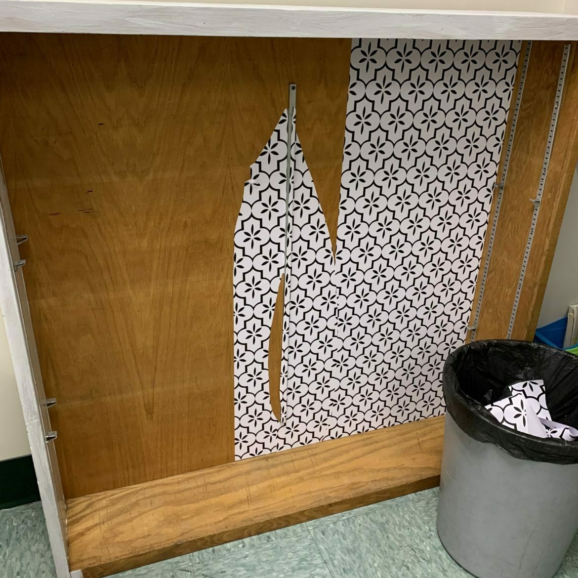 Wooden bookshelf with no shelves and peeled off white and blue patterned lining