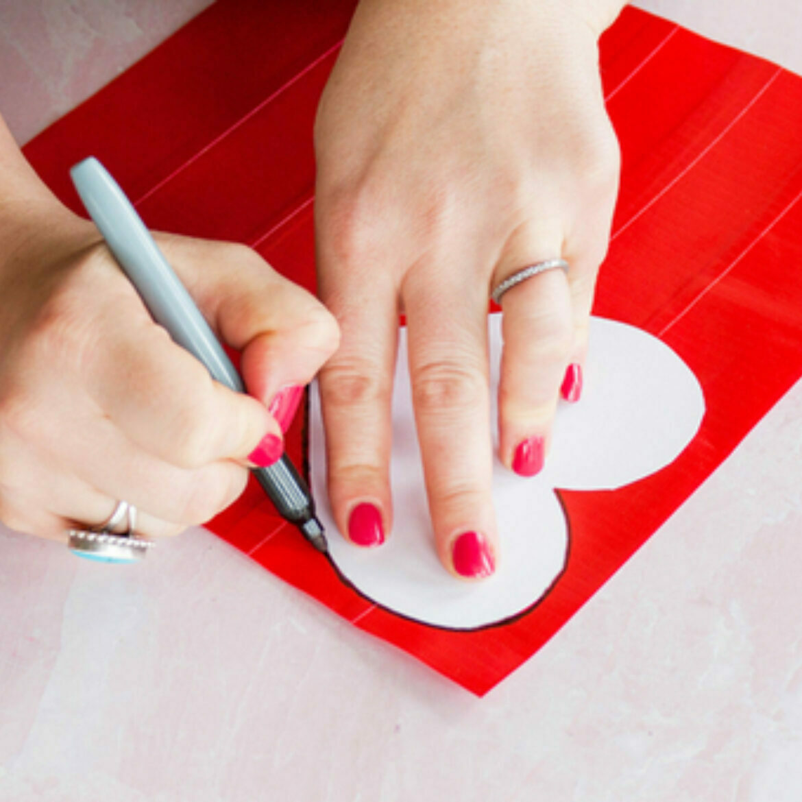 Two hands tracing a heart with a black marker on a sheet of duct tape