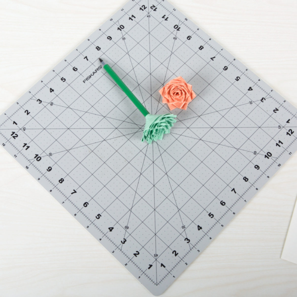 One green flower topping a pen and a pink flower placed on a crafting board