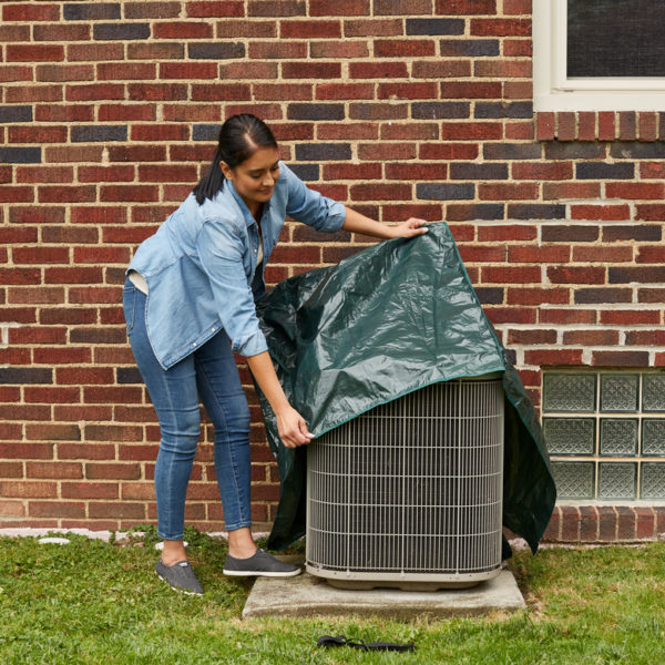 Woman installing AC cover on exterior AC unit.