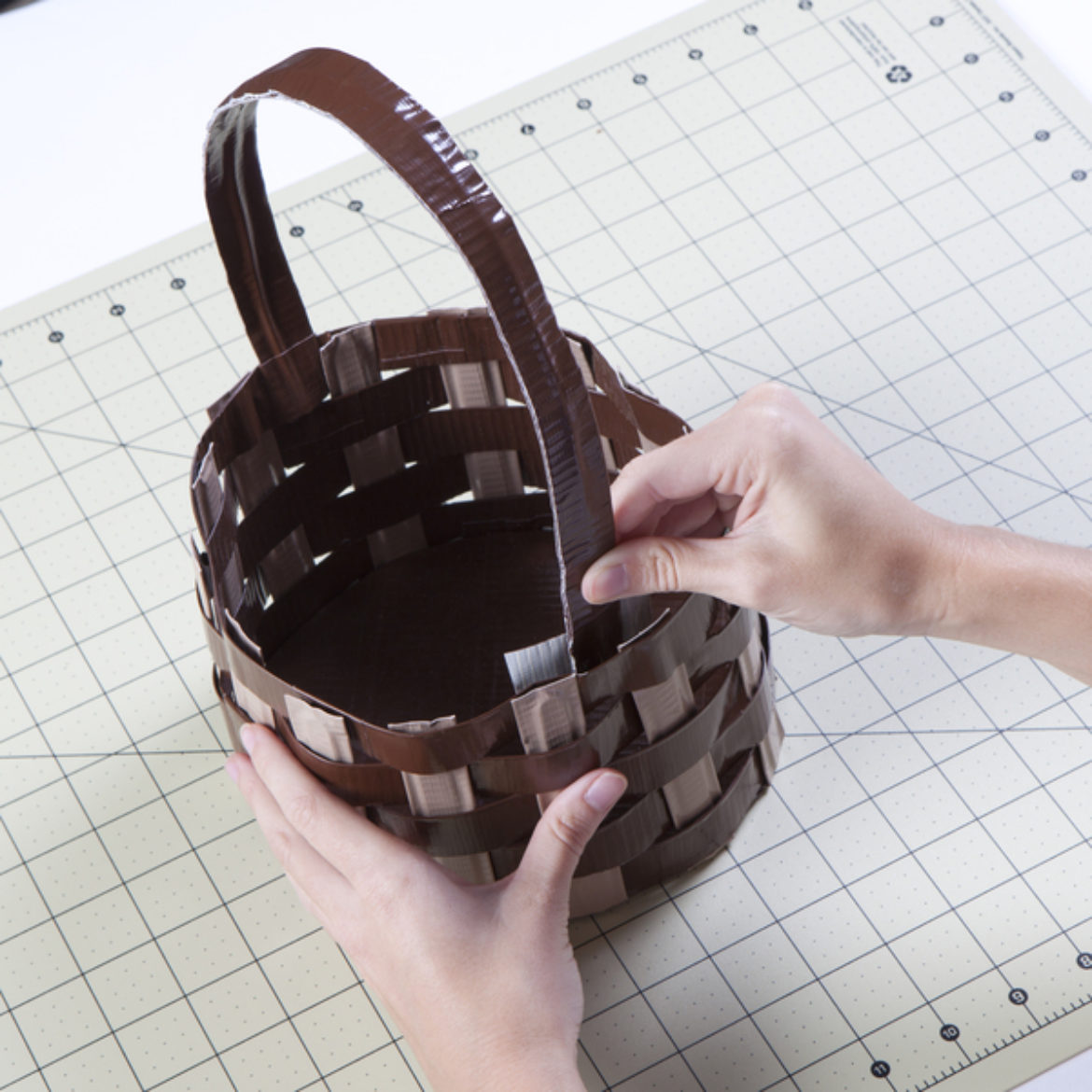 Handle fashioned from a double sided strip of Duck Tape being taped to the inside of the basket